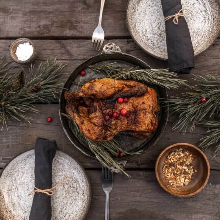 Roasted chicken on a wooden table with sprigs of holly.